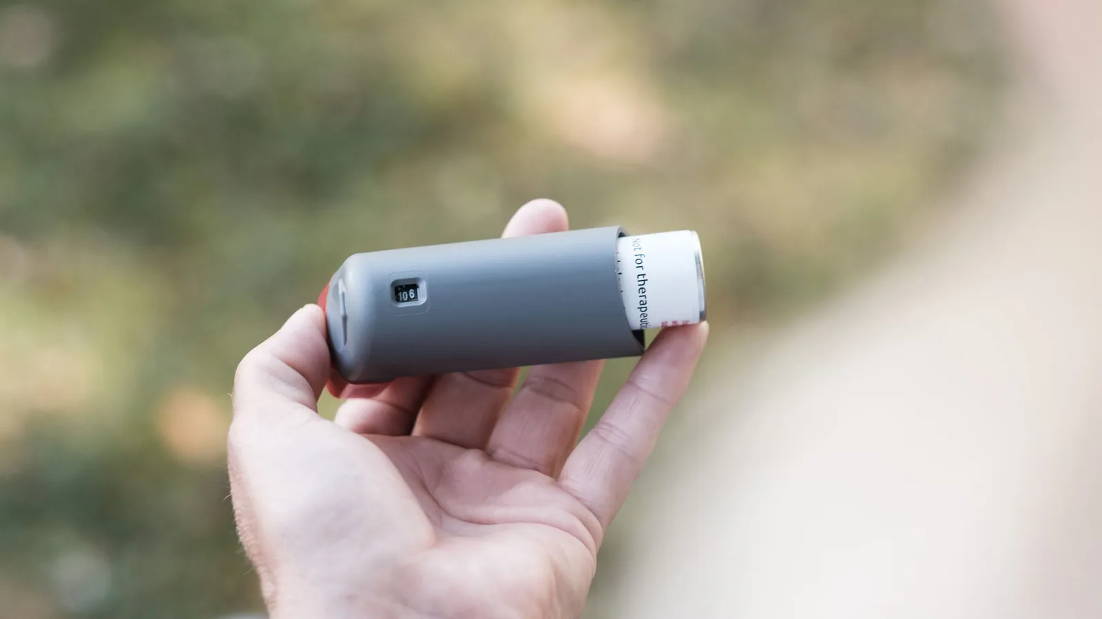 Mână ținând un inhalator pe fundalul unui spațiu verde